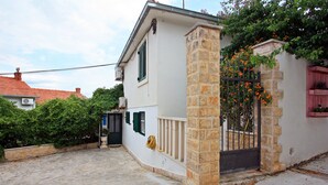 A house with a stone pillar, a gated entrance, and a small garden with orange flowers.