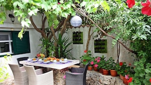 An outdoor patio with a table set for dining, surrounded by wicker chairs, potted plants, and a stone wall.