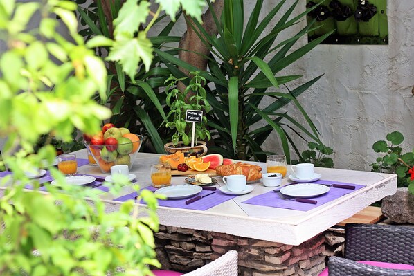 A breakfast table set outdoors with fruits, a croissant, and a sign that says "Water Please".