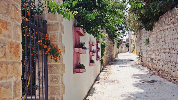 A narrow street with stone walls, a metal gate, and flower boxes on the walls.