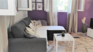 A modern living room with a grey sofa, a white coffee table, a flat-screen TV, and a small potted plant.