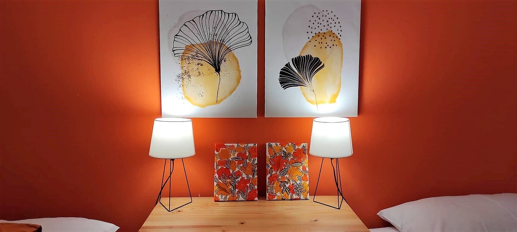 A room with two artworks on the wall, a wooden table with two lamps, and a floral-patterned side table.
