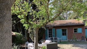 Ein rustikales Haus mit Ziegeldach, ein Garten mit Gartenmöbeln und ein großer Baum, der Schatten spendet.