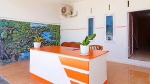 A reception desk with a white and orange design, a potted plant, and a mural on the wall.