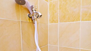 A shower with a handheld showerhead and a flexible hose against a yellow-tiled wall.