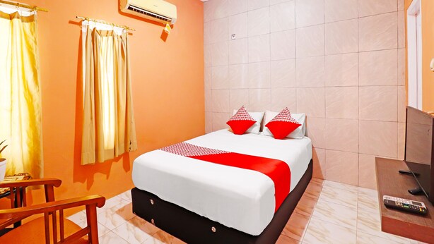 A hotel room with a bed, curtains, an air conditioning unit, a TV, and a remote control on a side table.