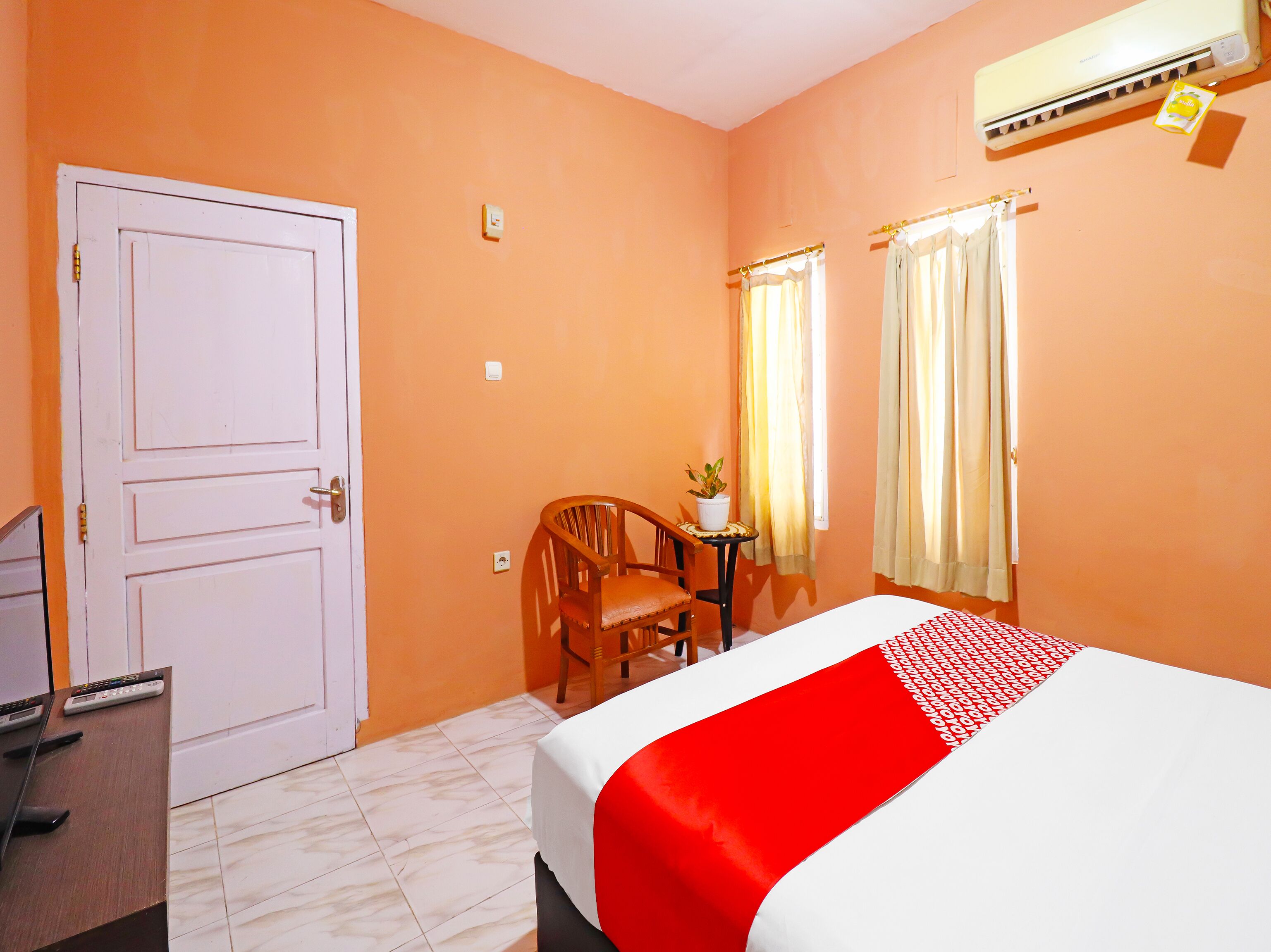 A hotel room with a bed, a desk with a chair, a potted plant, and a door.