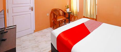 A hotel room with a bed, a desk with a chair, a potted plant, and a door.