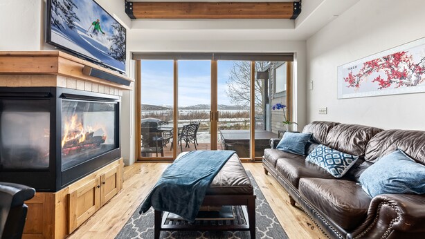 A cozy living room with a fireplace, a leather sofa, and a large window offering a view of the outdoors. - Newpark, Close to ski resorts and restaurants, Amazing Views, Private hot tub (Park City)