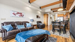 A spacious living room with a leather sofa, a dining area with wooden chairs, and a kitchen with wooden cabinets and a refrigerator. - Newpark, Close to ski resorts and restaurants, Amazing Views, Private hot tub (Park City)