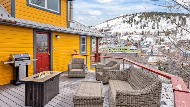 Une maison jaune dotée d’une terrasse aménagée avec des meubles en osier et un barbecue.