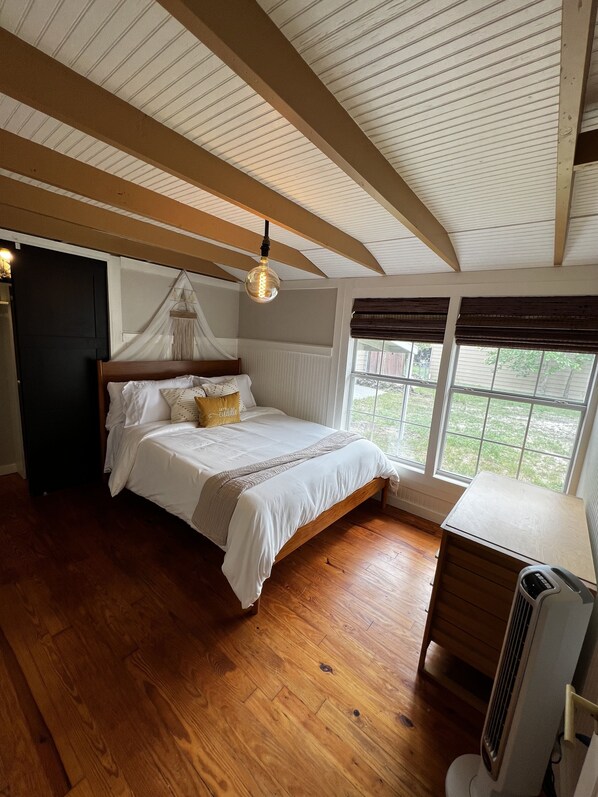 A bedroom with a wooden bed, a bedside table, a heater, and a window with blinds.
