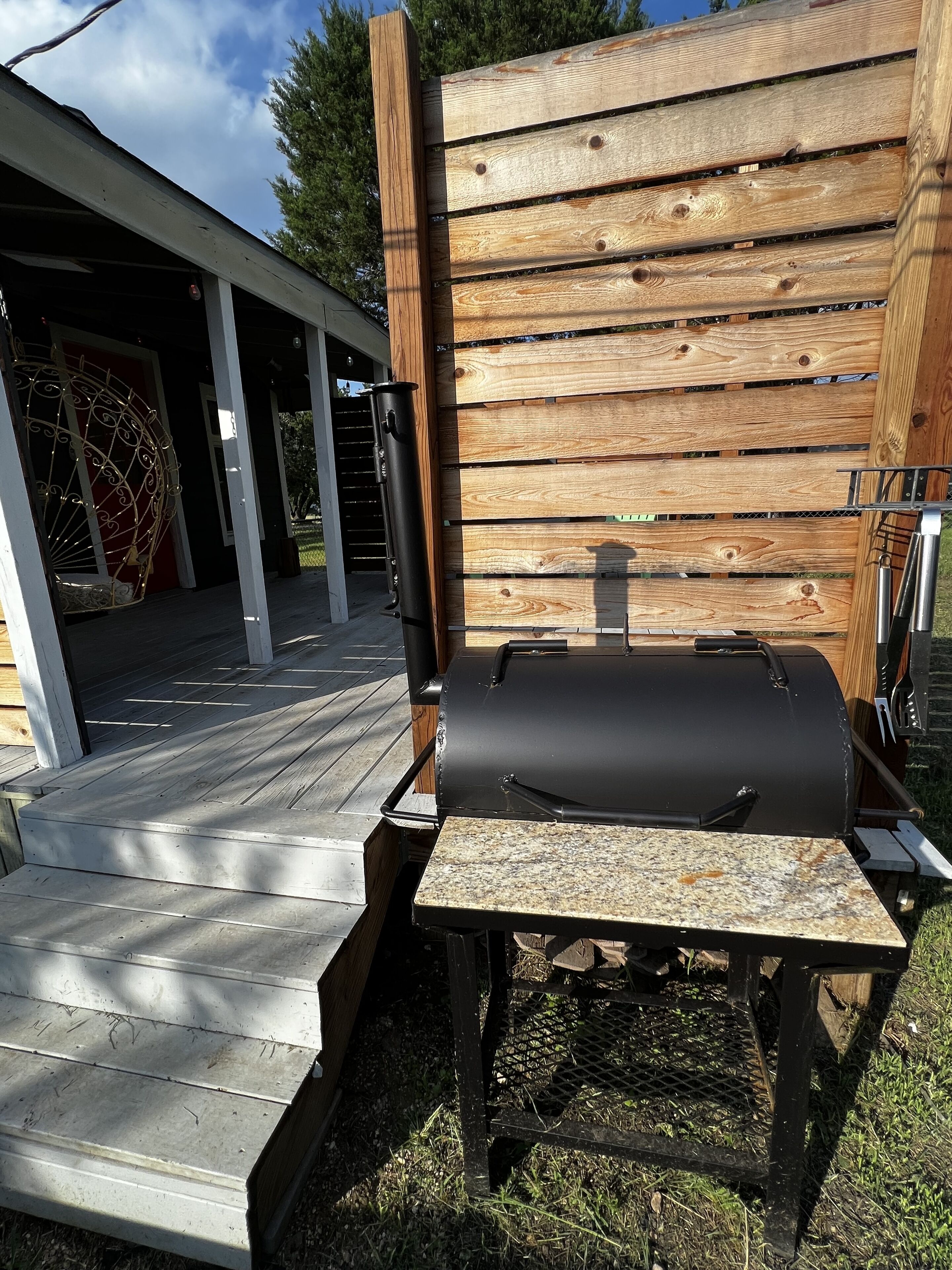A barbecue grill set up outdoors with a wooden fence and a covered patio area.