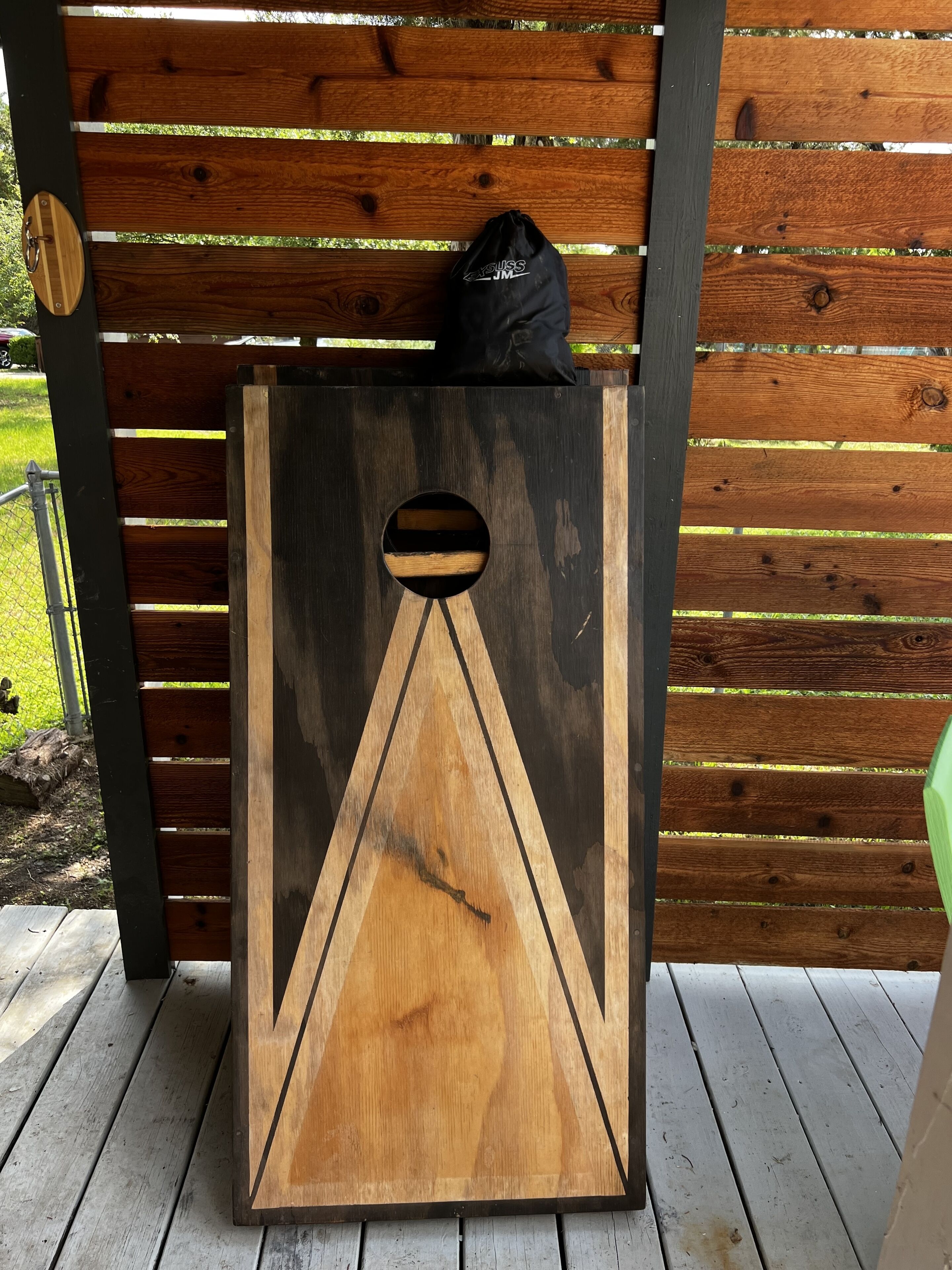 Eine Holzkonstruktion mit geometrischem Muster, vielleicht ein dekoratives Element oder ein Möbelstück, vor einem Hintergrund aus Holzzaun.