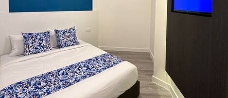 Un dormitorio moderno con una cama grande, una pared de acento azul, un televisor montado y una pintura de cielo nocturno.