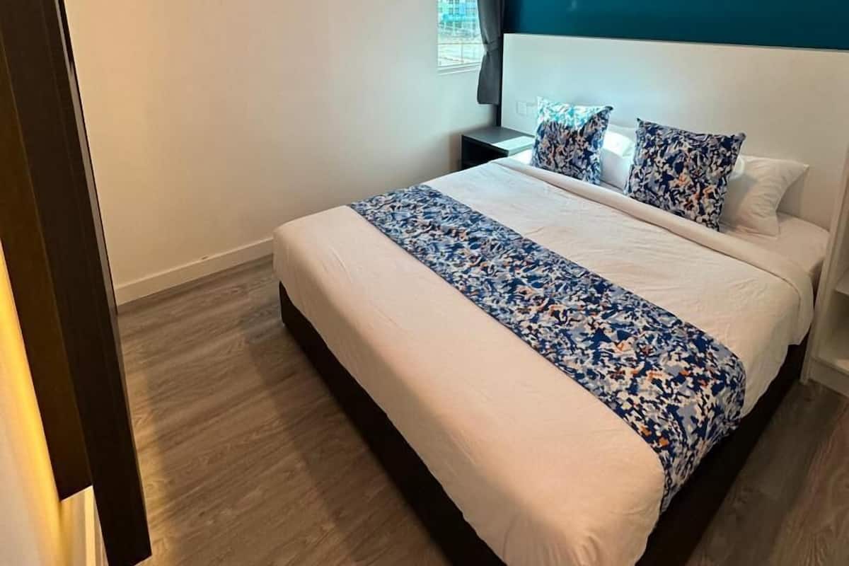 Een moderne hotelkamer met een groot bed, nachtkastje, raam met gordijnen en een blauwe accentmuur.