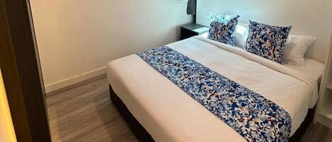 Habitación de hotel moderna con una cama grande, una mesita de noche, un ventanal con cortinas y una pared azul de acento.