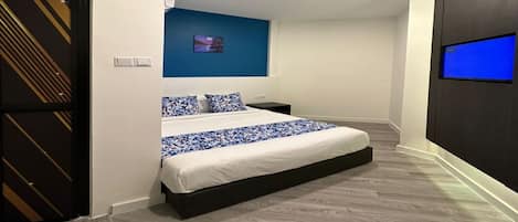 A modern hotel room with a large bed, a flat-screen TV, and a blue accent wall.
