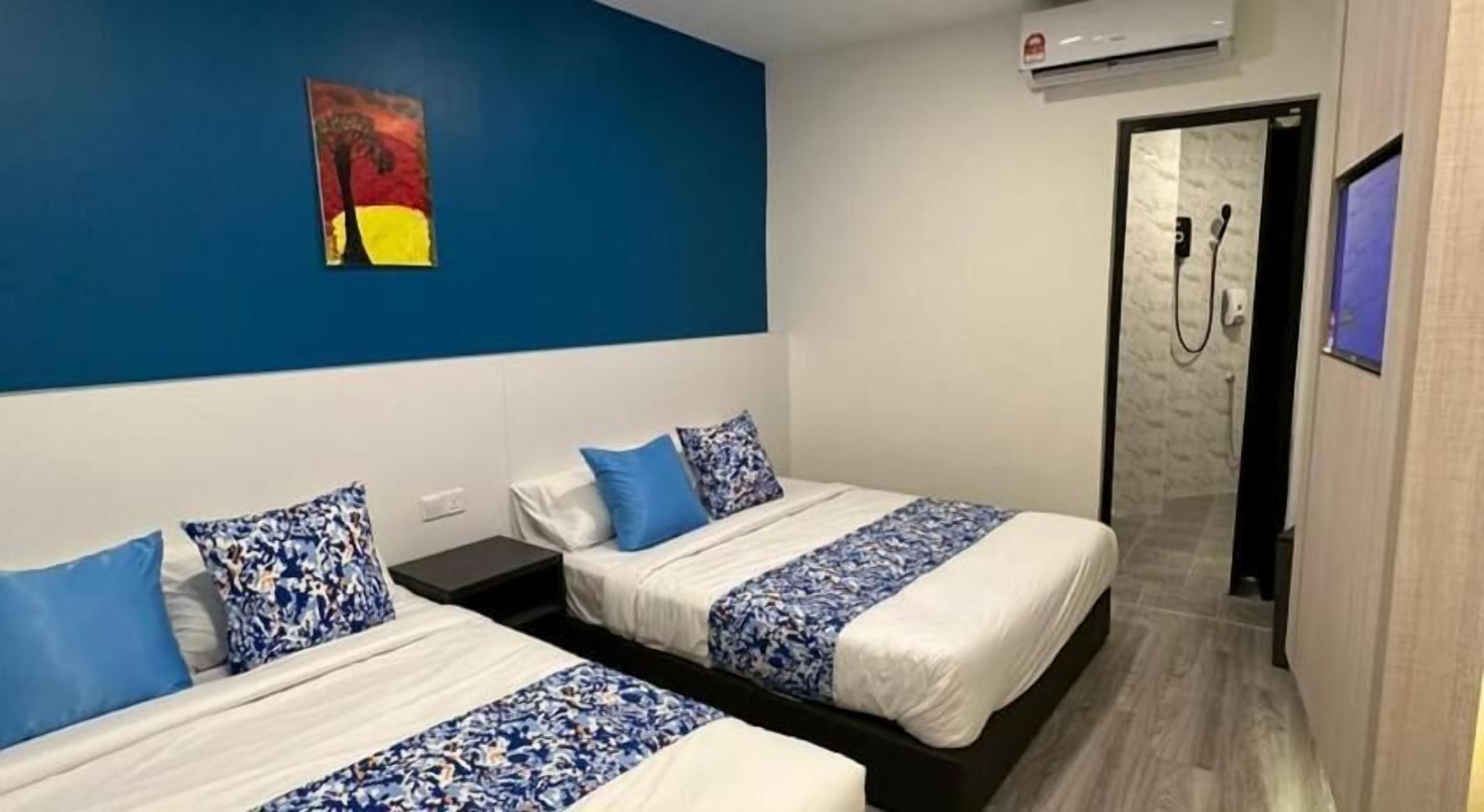 Habitación de hotel con dos camas, una pared azul decorativa, un cuadro y zona de ducha.