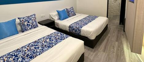 A modern hotel room with two beds, a blue accent wall, and a shower area.