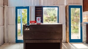 Una habitación con un escritorio de madera, una ventana con marco azul y vistas al verdor exterior.