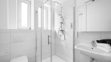 A modern bathroom with a glass-enclosed shower, a white sink, and a toilet.