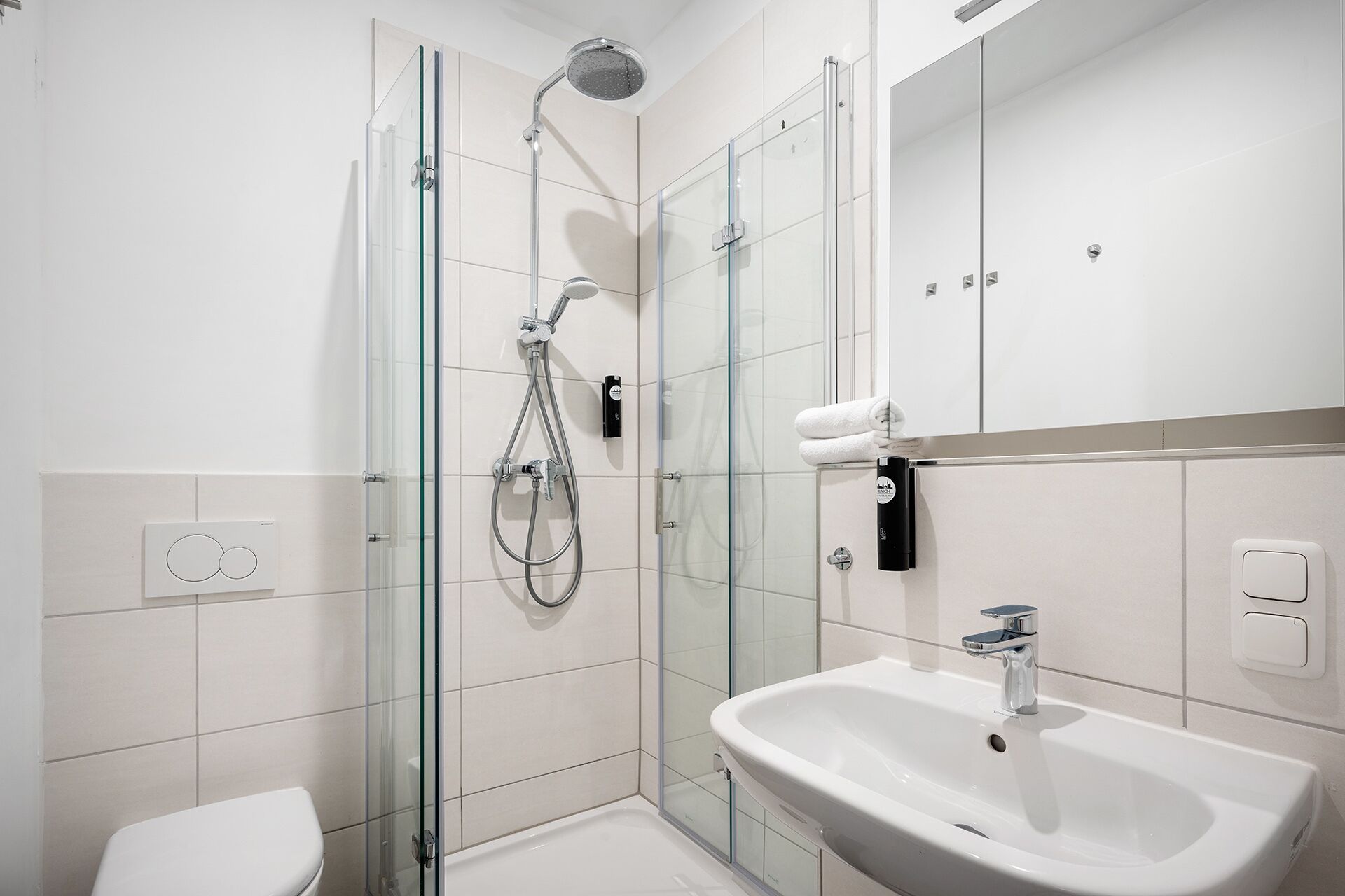 Un baño moderno con cabina de ducha de vidrio, un lavamanos blanco y un inodoro.