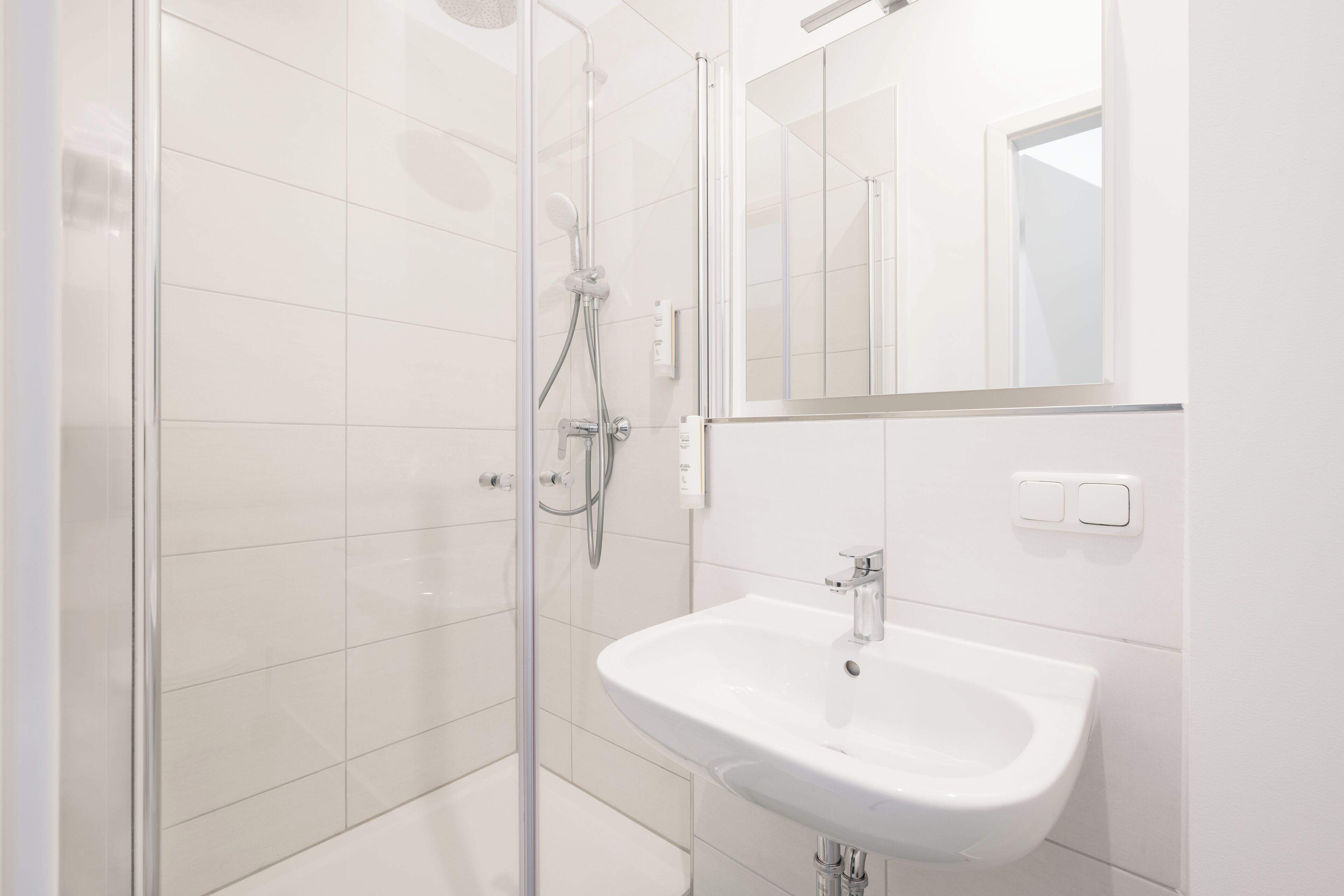 Un baño moderno con cabina de ducha de vidrio, un lavabo blanco y un espejo sobre el lavabo.