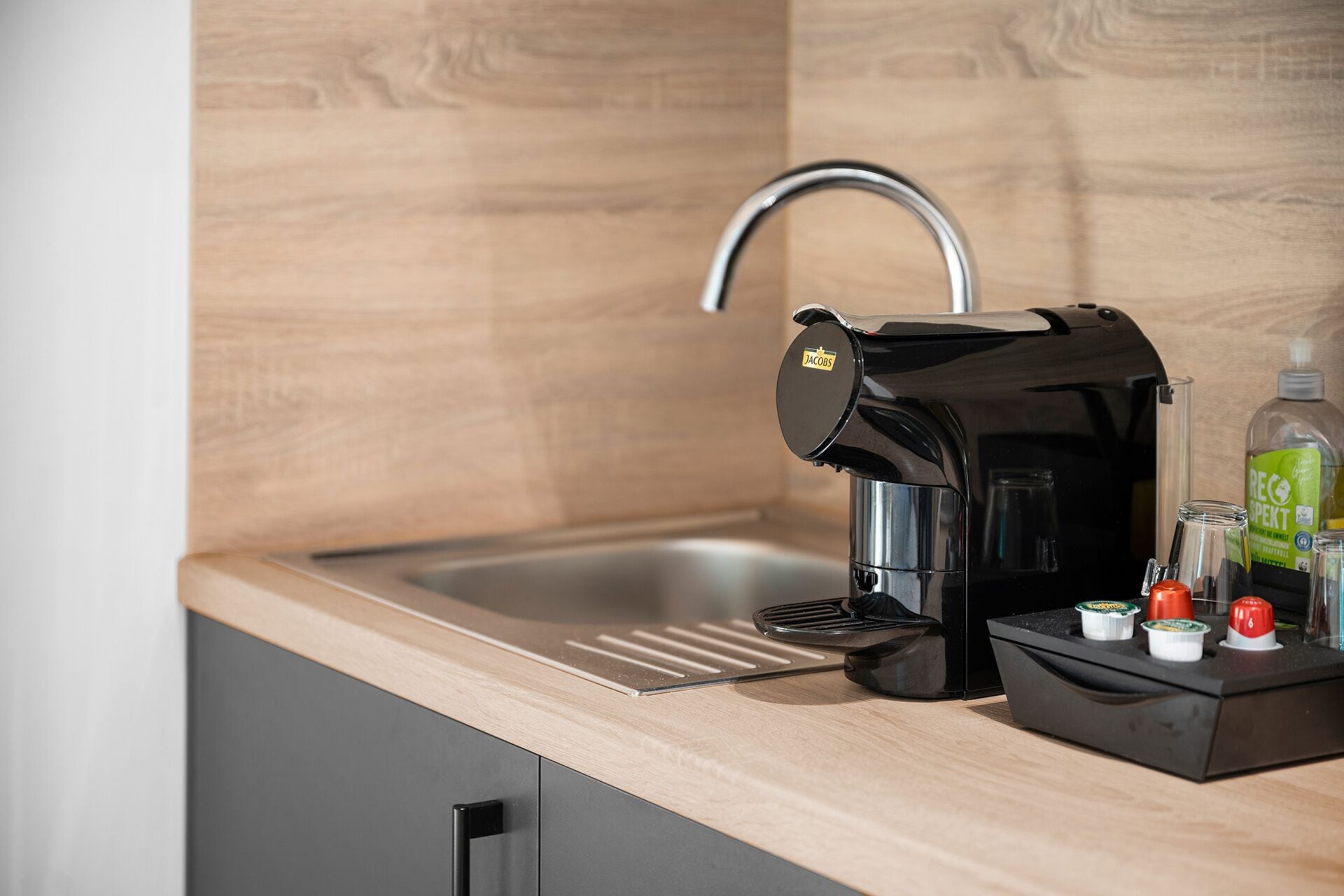 Una cuina moderna amb un rentaplat amb encastrament, una cafetera i un suport per a càpsules de cafè.