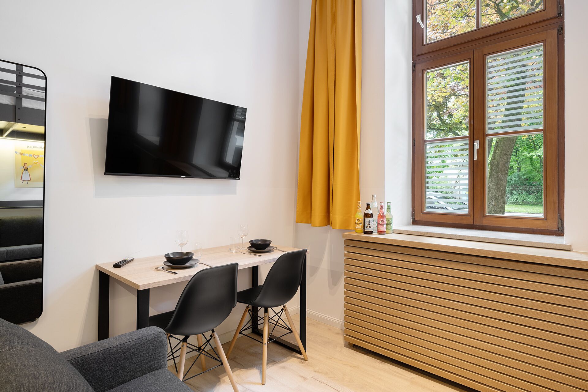 A modern living room with a flat-screen TV, a dining table with chairs, a sofa, and a window with blinds.