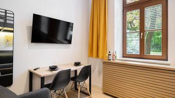 A modern living room with a flat-screen TV, a dining table with chairs, a sofa, and a window with blinds.