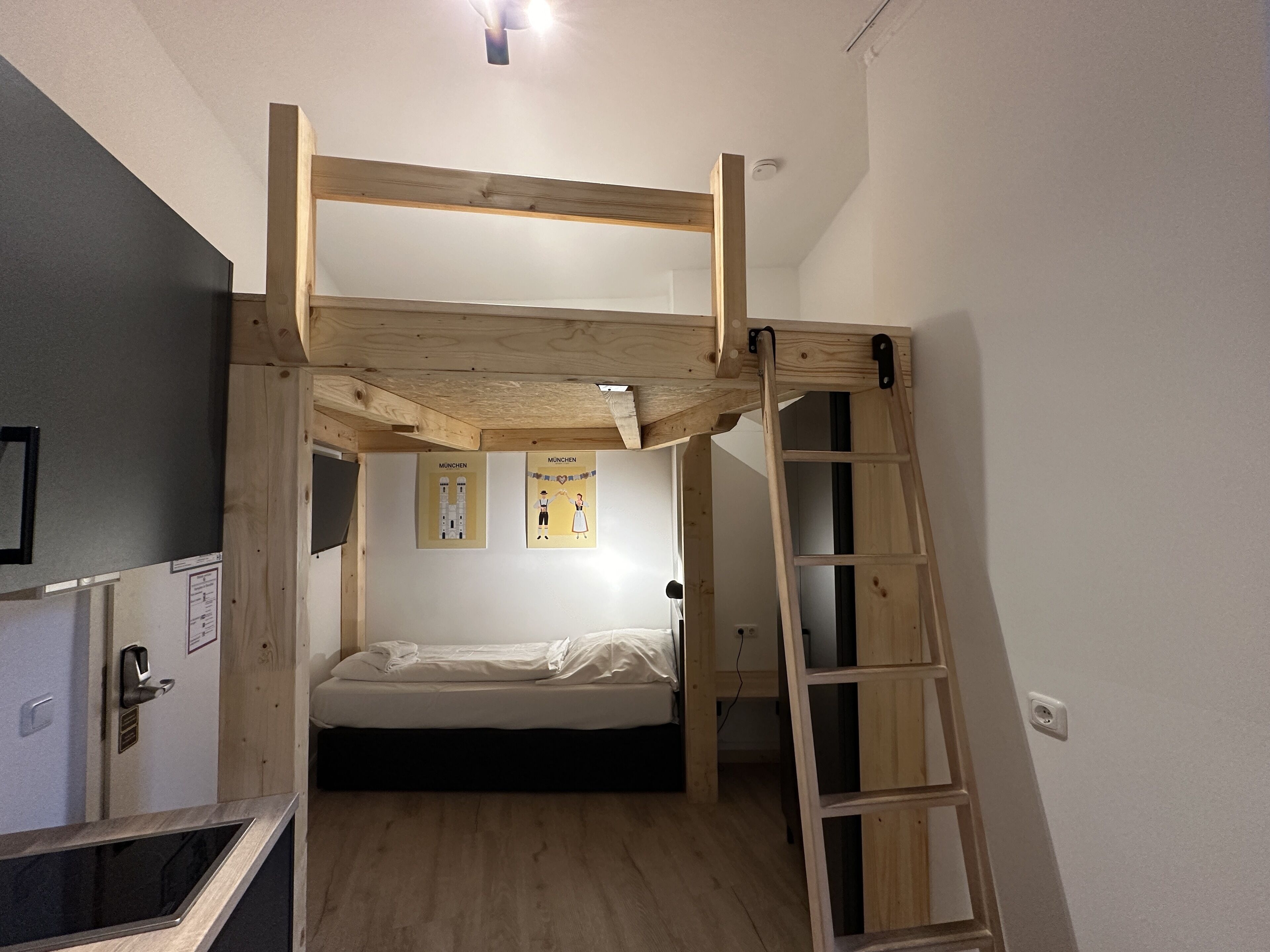A bunk bed room with a wooden ladder, a desk, and two framed pictures on the wall.