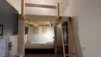A bunk bed room with a wooden ladder, a desk, and two framed pictures on the wall.