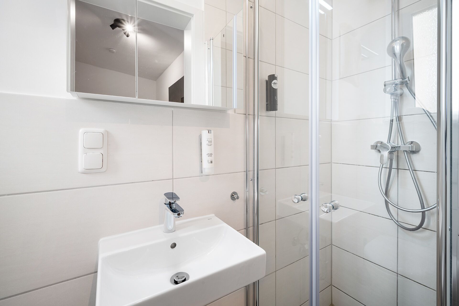 Ein modernes Badezimmer mit einem weißen Waschbecken, einer Duschkabine aus Glas und einem Spiegel über dem Waschbecken.