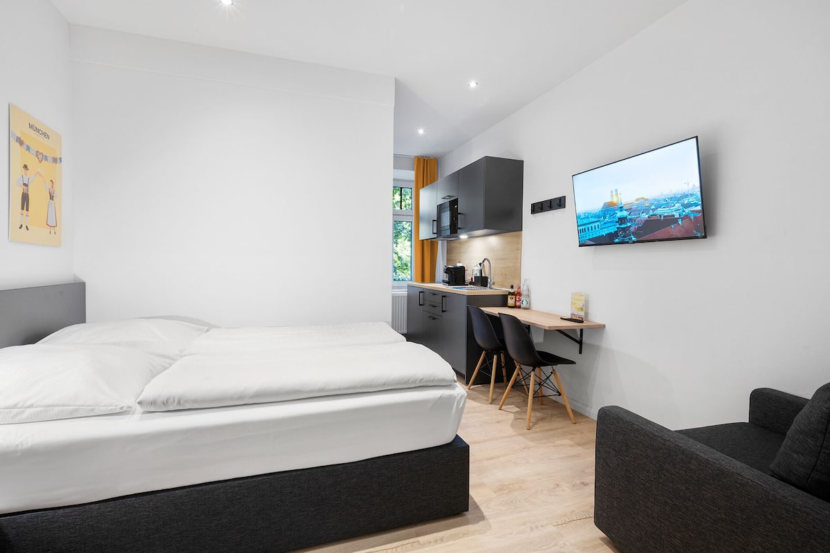 Une chambre d’hôtel moderne équipée d’un lit, d’un bureau, d’une chaise et d’un téléviseur diffusant une vue sur la ville.