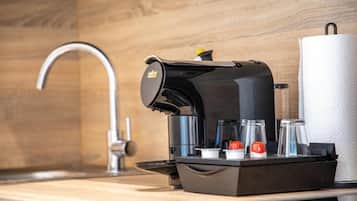 Una cafetera moderna con depósito de agua, cápsulas de café y dispensador de toallas de papel sobre una encimera de madera.
