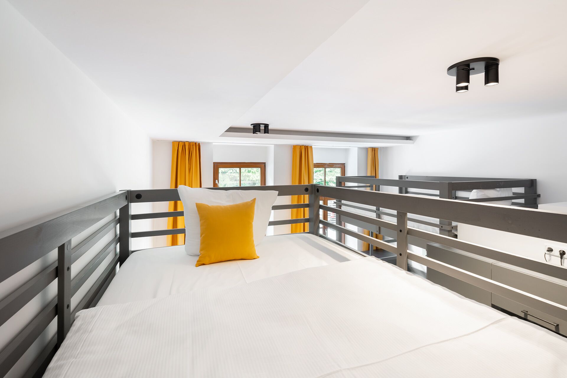 Habitació d'hotel moderna amb un llit superposat, una petita finestra amb cortines i un lluminari al sostre.