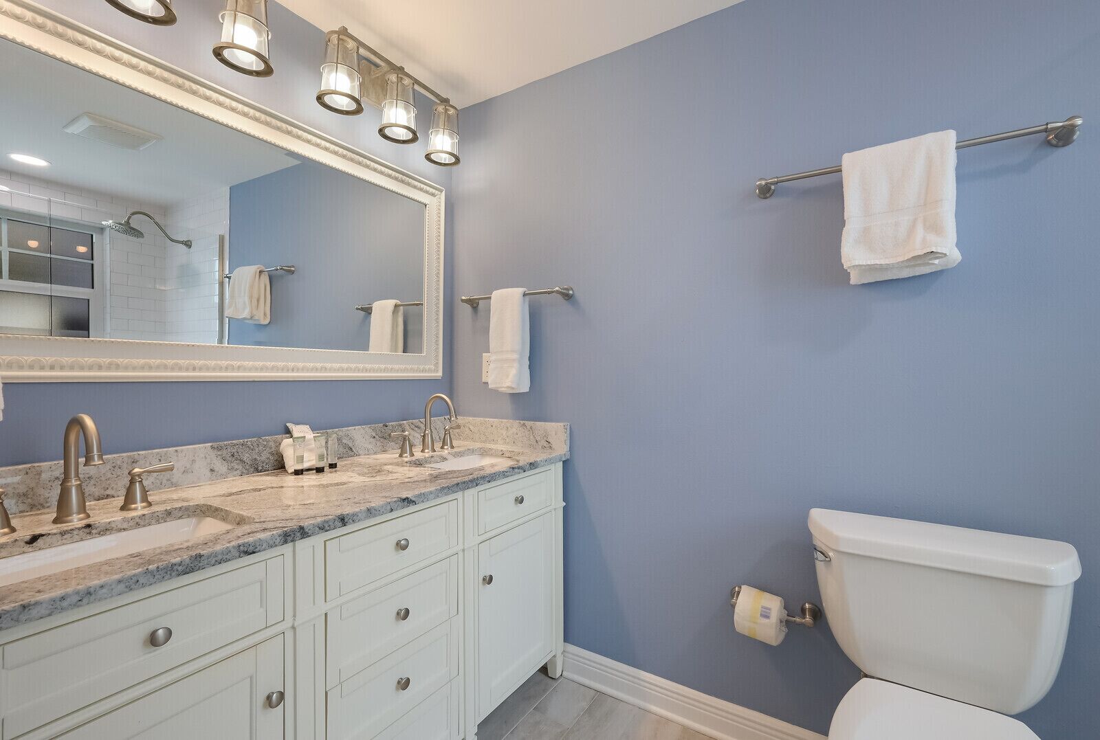 A bathroom with a double sink vanity, a toilet, and a towel rack.
