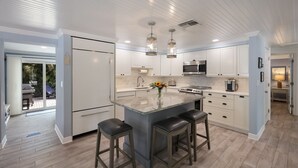 Une cuisine moderne avec des meubles blancs, un îlot central doté de tabourets, des appareils en acier inoxydable et un éclairage suspendu.
