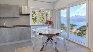 Une cuisine moderne avec un coin repas, de grandes fenêtres offrant une vue sur les montagnes et un lac, et un vase rempli de fleurs sur la table.