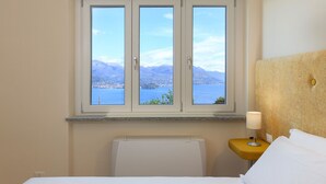 Une chambre d’hôtel avec un lit, une table de chevet, une lampe et une fenêtre donnant sur un lac et des montagnes.