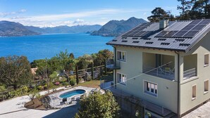 Une maison à deux étages avec une piscine, des panneaux solaires sur le toit et une vue sur un lac et des montagnes.