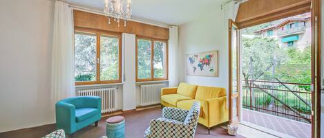 A living room with a blue armchair, a patterned armchair, a yellow sofa, and a chandelier.