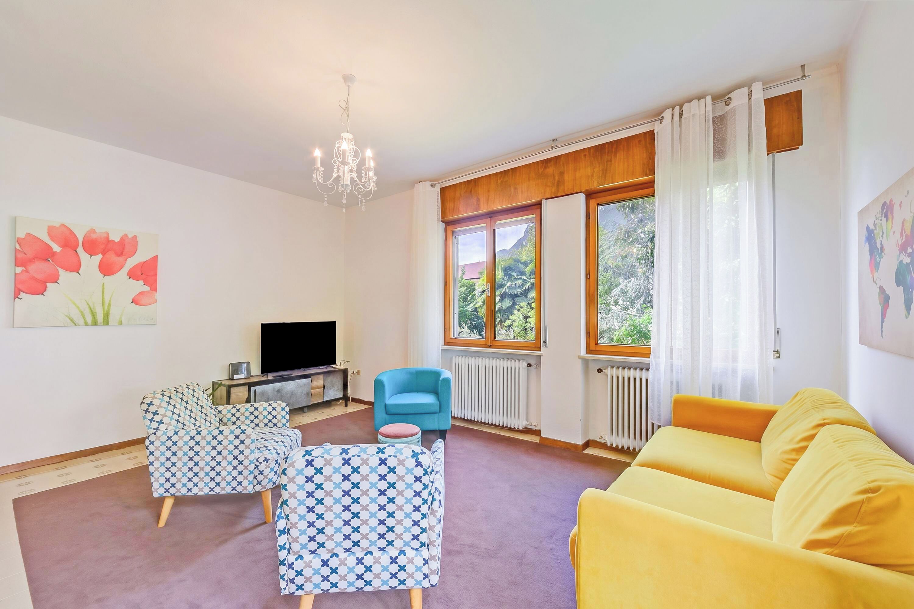 A living room with a sofa, two patterned chairs, a television, and a chandelier.