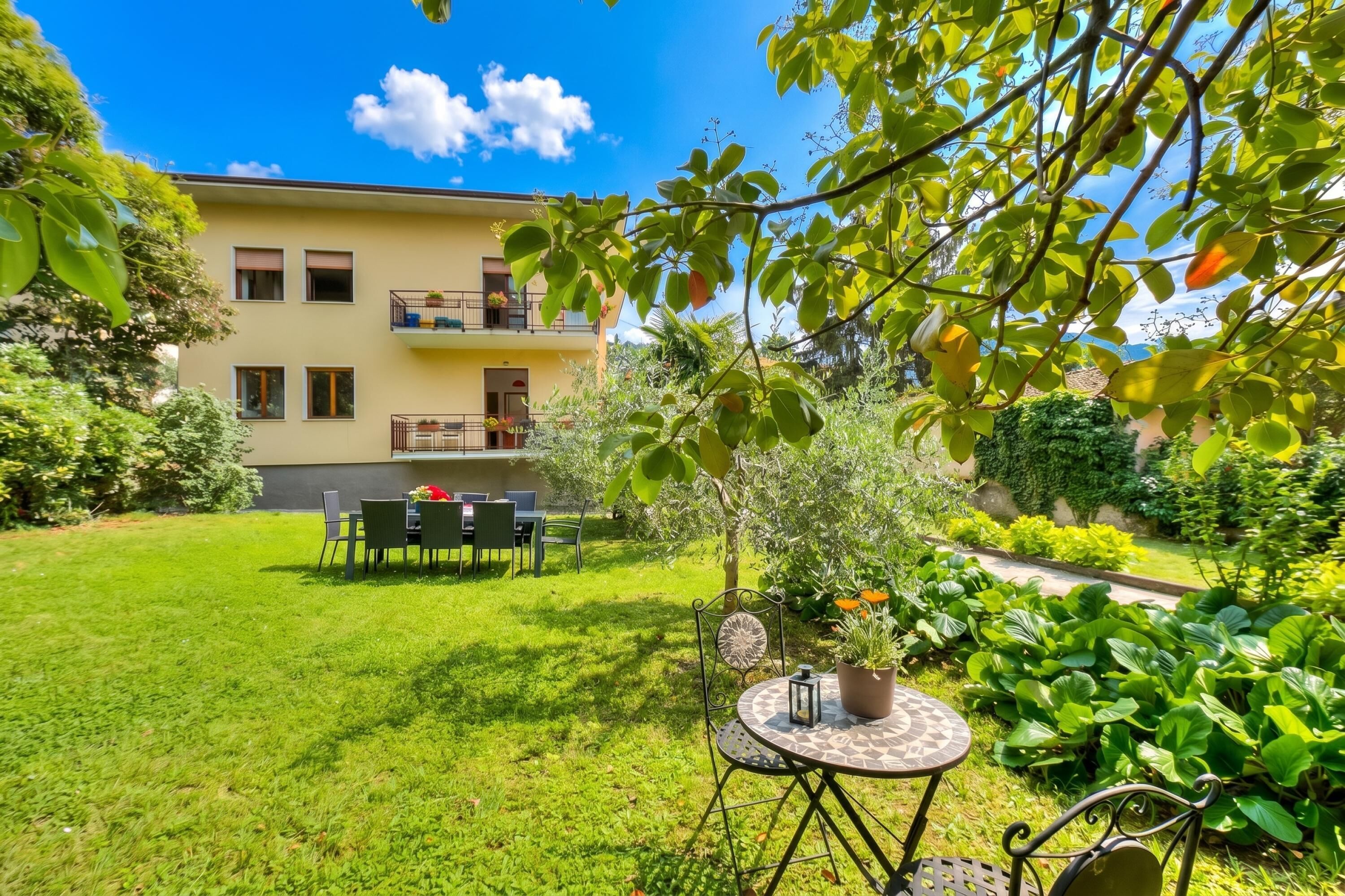 A two-story building with a balcony, a well-maintained lawn, and a table with chairs.