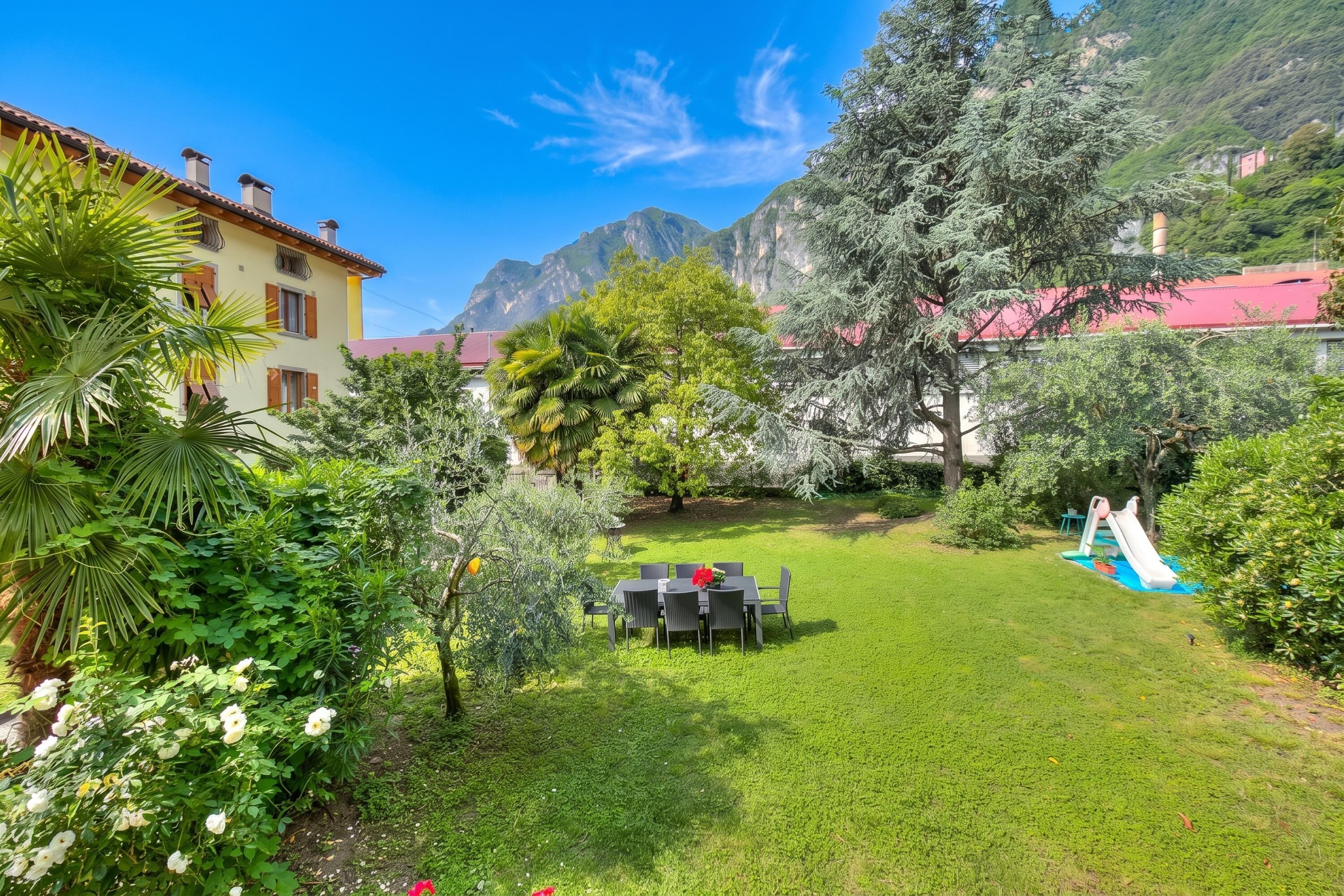 A garden with a dining table, a slide, and a mountain backdrop.