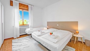 Habitación de hotel con dos camas, un radiador, una ventana con cortinas, una mesita con lámpara y una alfombra estampada.