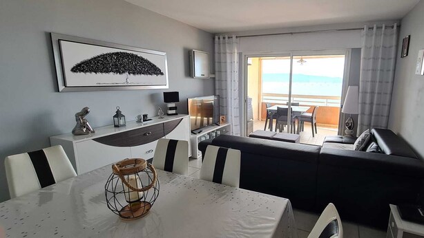 Un salon moderne avec une table blanche, des chaises à rayures noires et blanches, un canapé noir et un balcon avec vue.