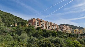 Un immeuble résidentiel à plusieurs étages, doté de balcons, situé sur une colline et entouré d’une végétation luxuriante.