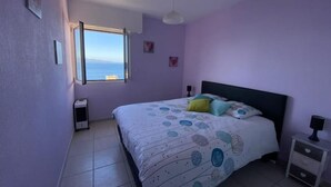 Une chambre à coucher avec un lit, une table de chevet, une fenêtre et une vue sur la mer.